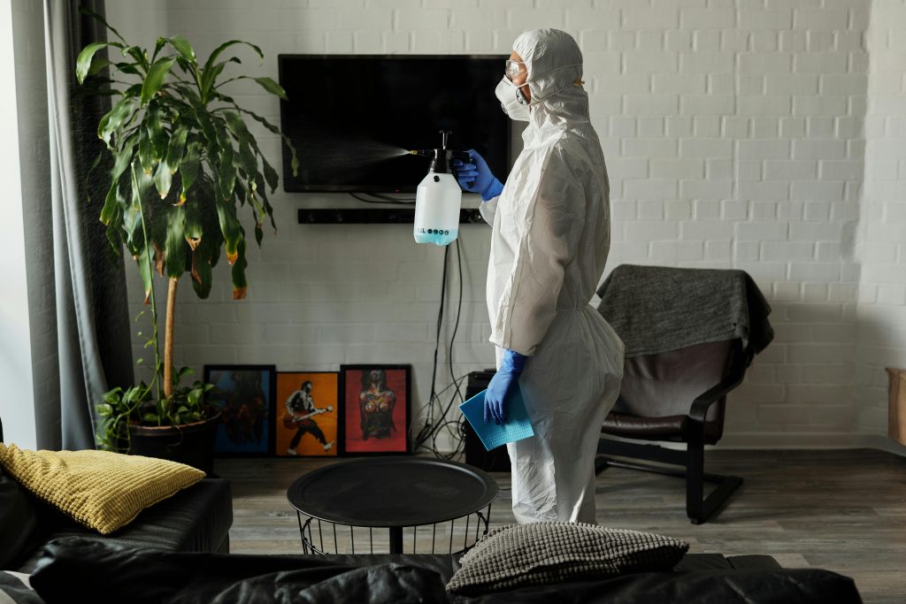 A person wearing PPE disinfects a living room for safety measures.